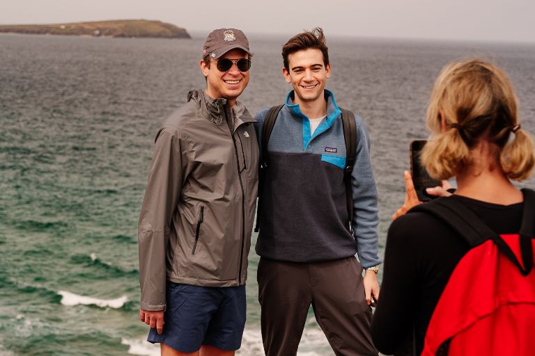 Two people pose for a picture against a coastal backdrop