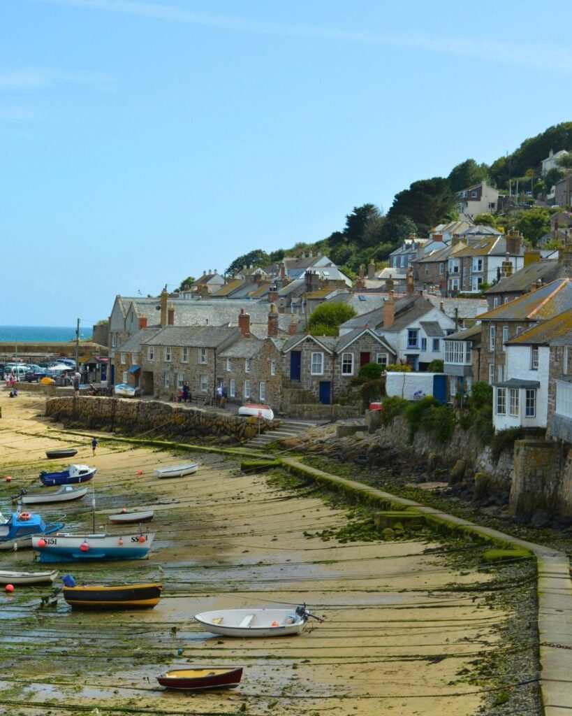 Coastal village with stone cottages along a harbor and small boats resting on the wet beach.